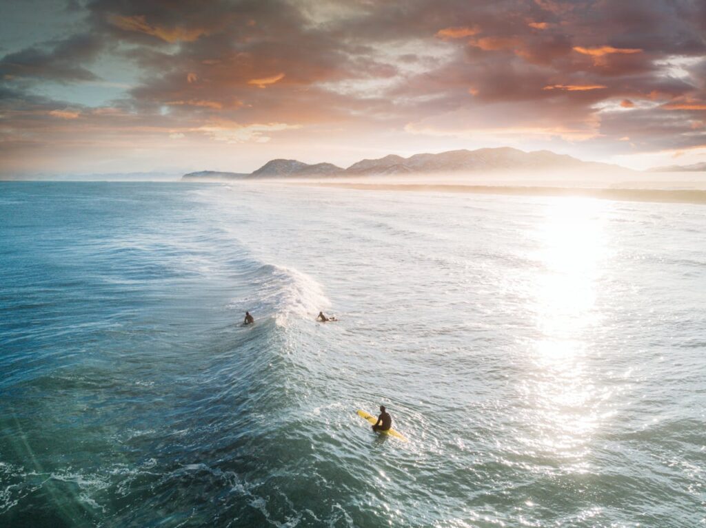 Three surfers riding waves under a stunning sunset in Kamchatka, Russia's coastline.